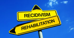 The words Recidivism and Rehabilitation on yellow arrow sign
