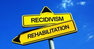 The words Recidivism and Rehabilitation on yellow arrow sign