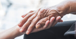 Older person's hand being held by carer