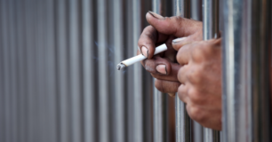 Image of two hands through prison bars, one hand holding a lit cigarette