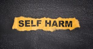 Image of a black background, with yellow torn paper the words Self Harm on in black letters