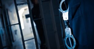 Image of a prisoner behind bars and a prison guard with handcuffs attached to his belt