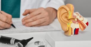 Image of a consultant audiologist sitting at desk with hearings aids, otoscope and a cast of an ear.