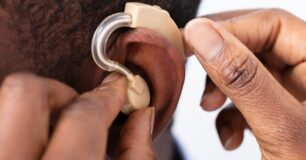 Image of a doctor's hands close up, inserting a hearing aid into a patient's ear.