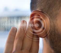 Image of a young man holding his ear trying to hear better.