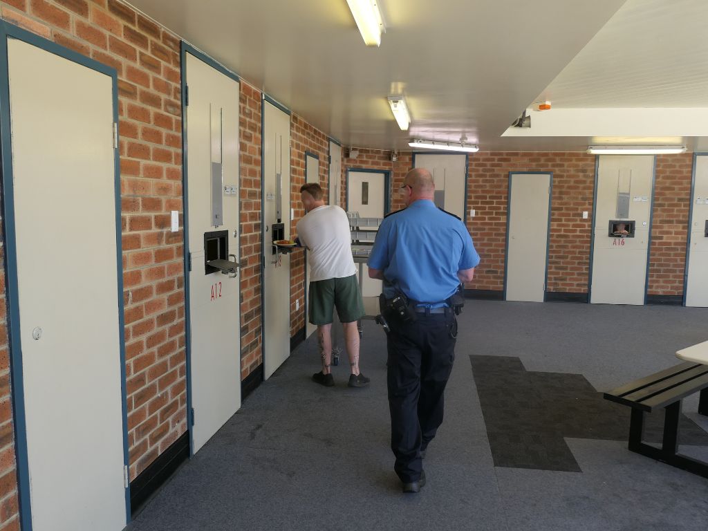 Image of a prisoner serving food to prisoners through cell door hatches, in Hakea Prison