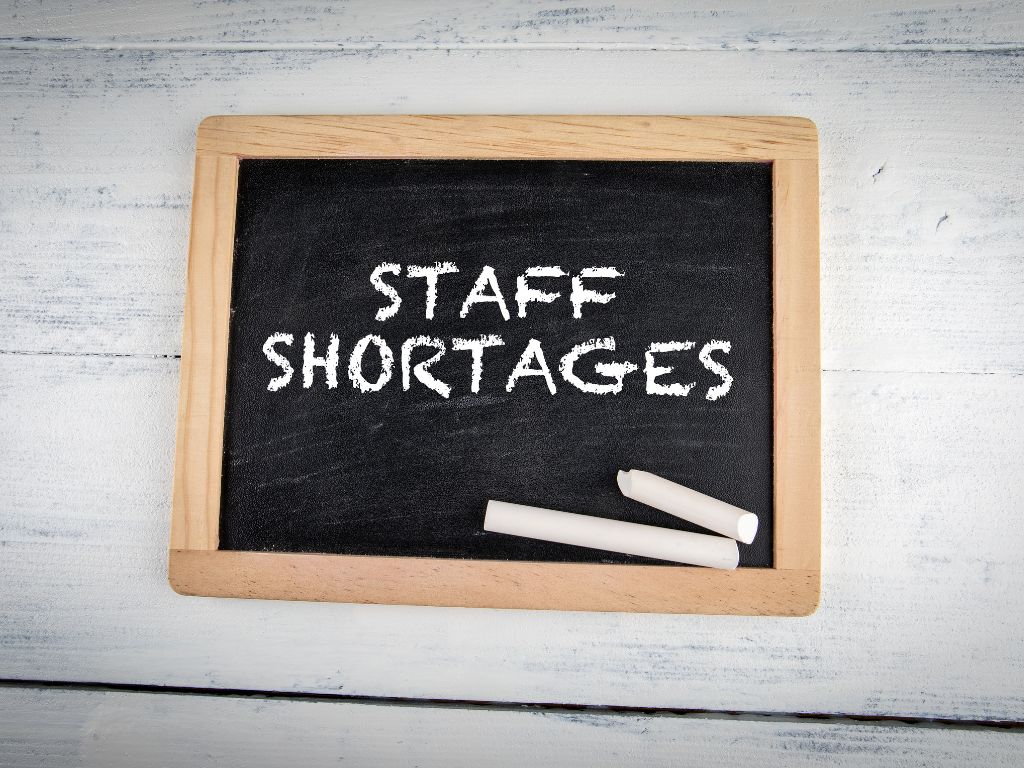 Image of a handheld chalkboard with the wording 'Staff Shortages' on.